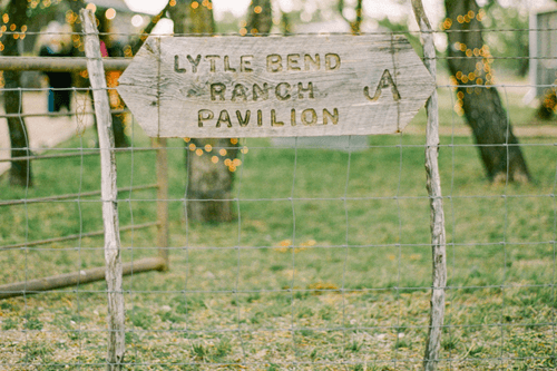 a wooden sign is sitting on top of a fence in a field .