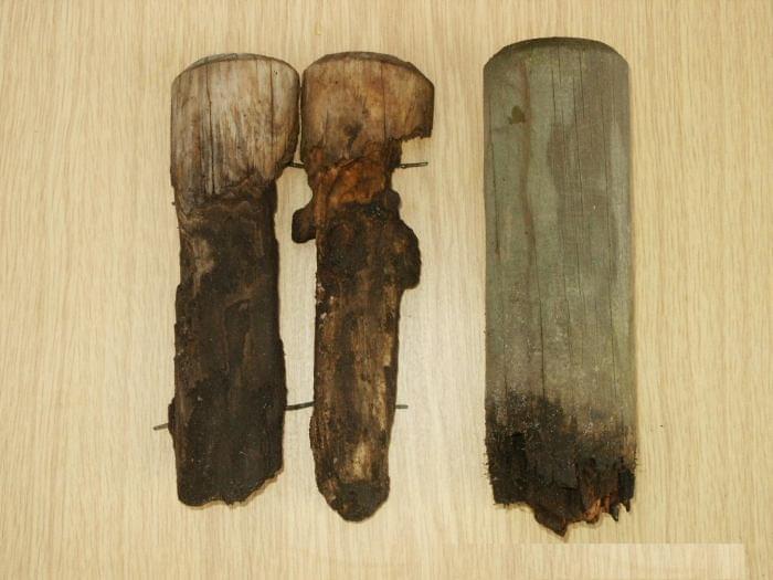 Drei verwitterte Holzpfosten in verschiedenen Formen und Farben auf einer Holzfläche.