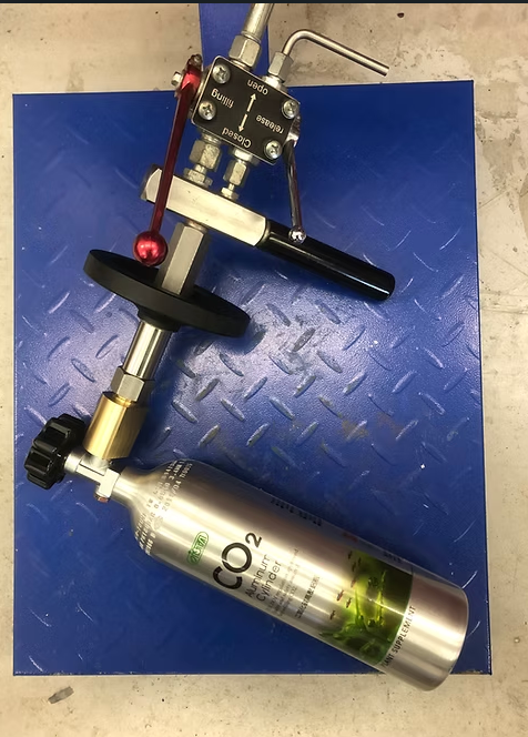 CO2 tank with regulator, valve, and handle on a blue metal surface.