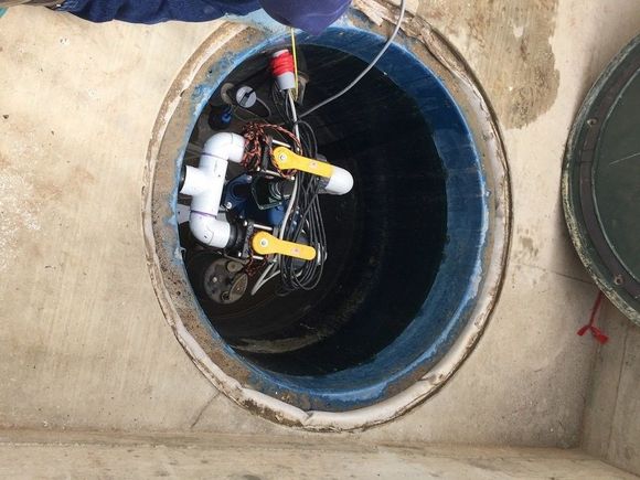 Blue tank and white hoses inside a concrete utility pit.