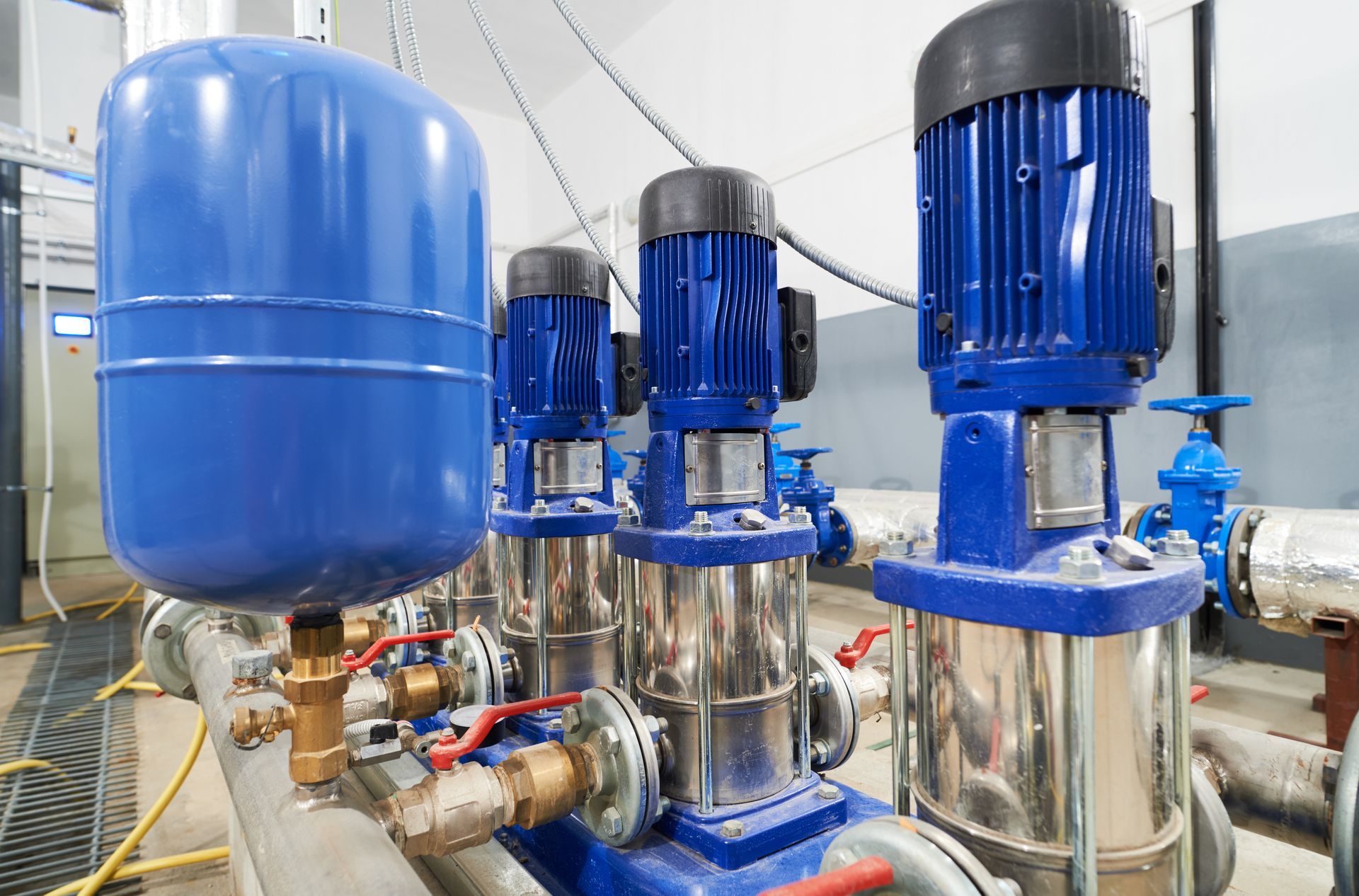 Industrial pumps and blue tanks in a stainless-steel mechanical room