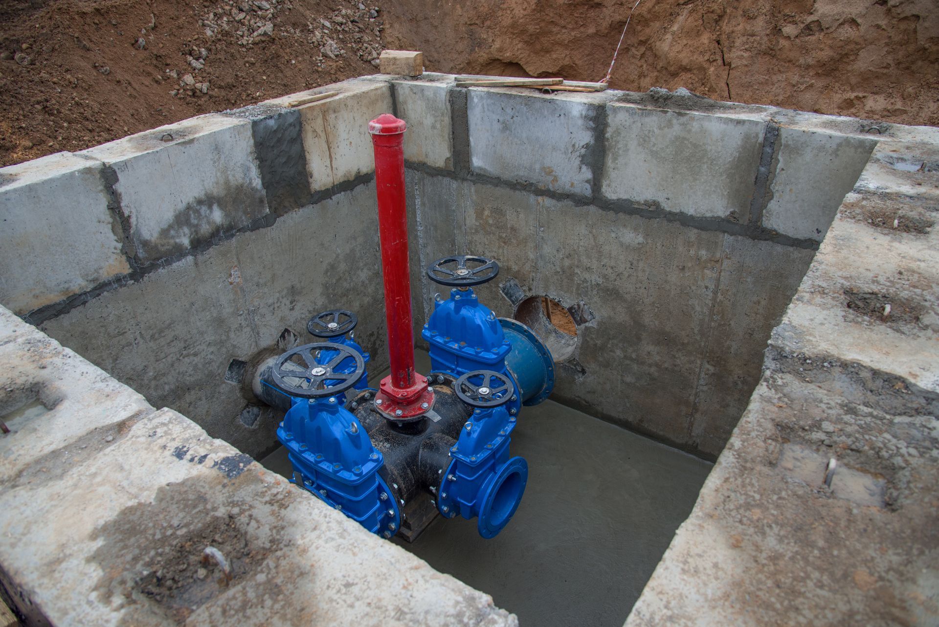 Blue water valves and a red pipe inside a concrete utility pit.