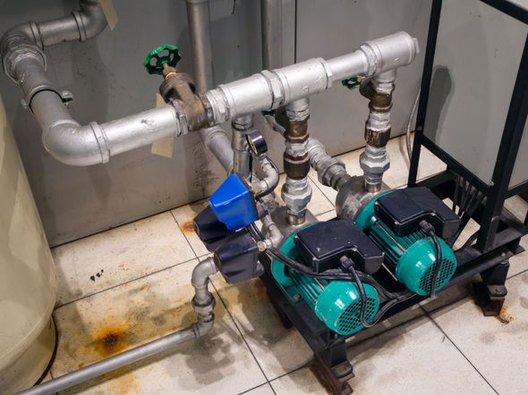Green industrial pump and motor assembly on a concrete base, with orange piping in a dim workshop.