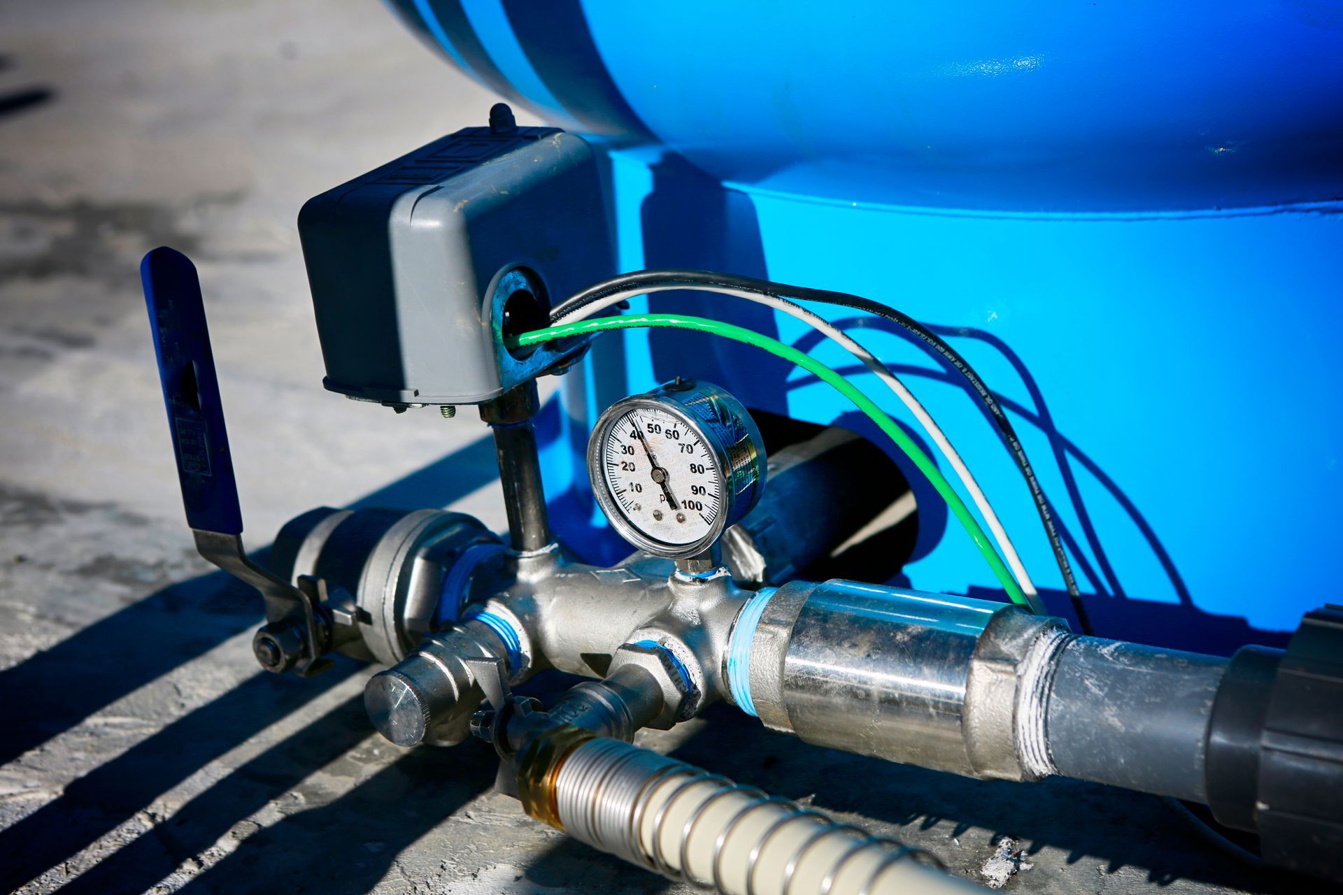 Blue industrial piping with pressure gauge and valves attached to a tank