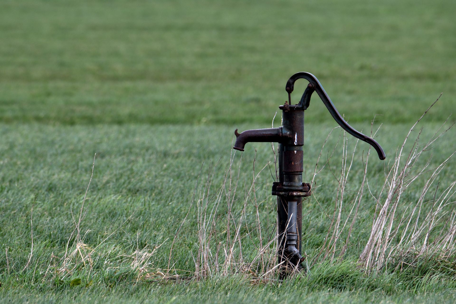 Old black water hand pump in a grassy field