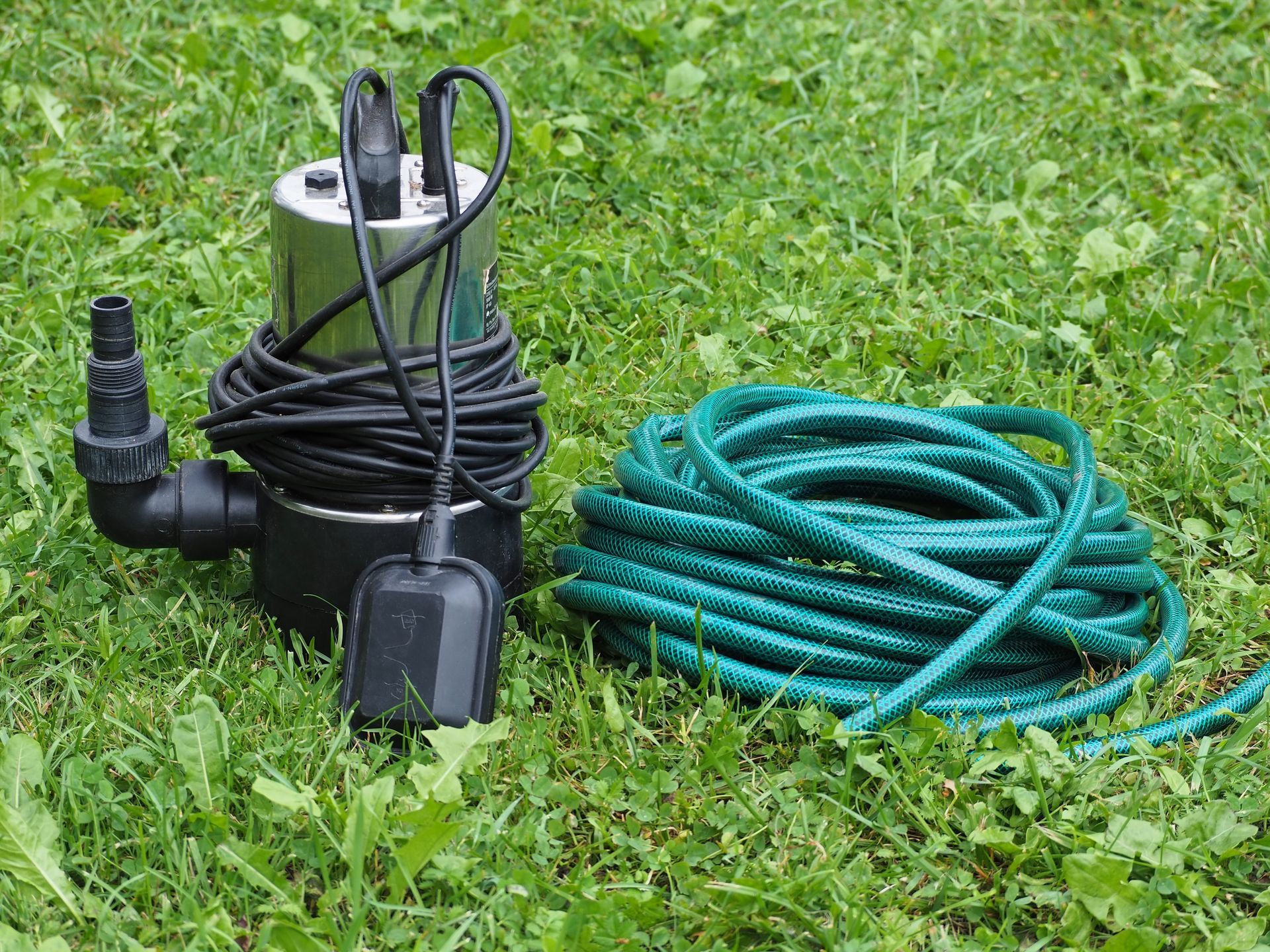 Submersible pump with coiled green hose on grass outdoors