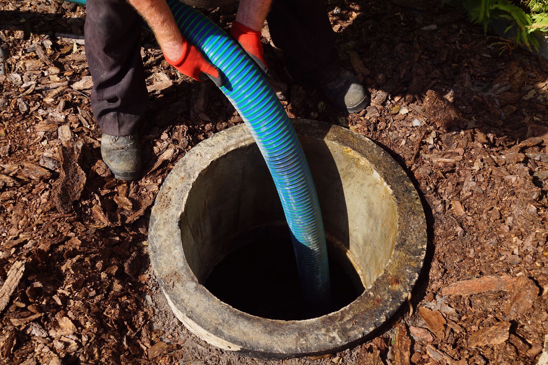Person using a blue hose to drain water into a concrete well opening outdoors