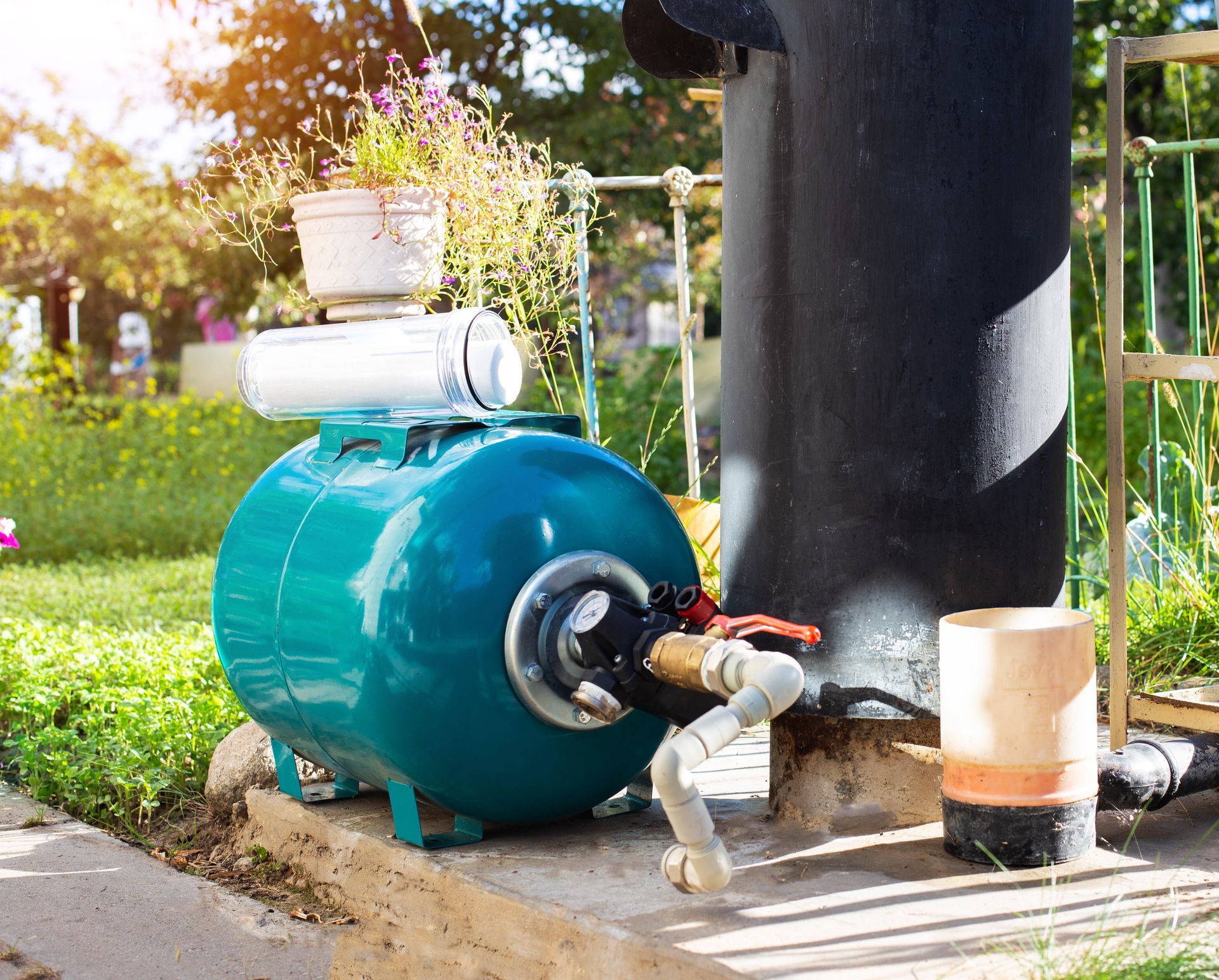 Turquoise industrial tank with pipes beside a black utility pole on a sidewalk