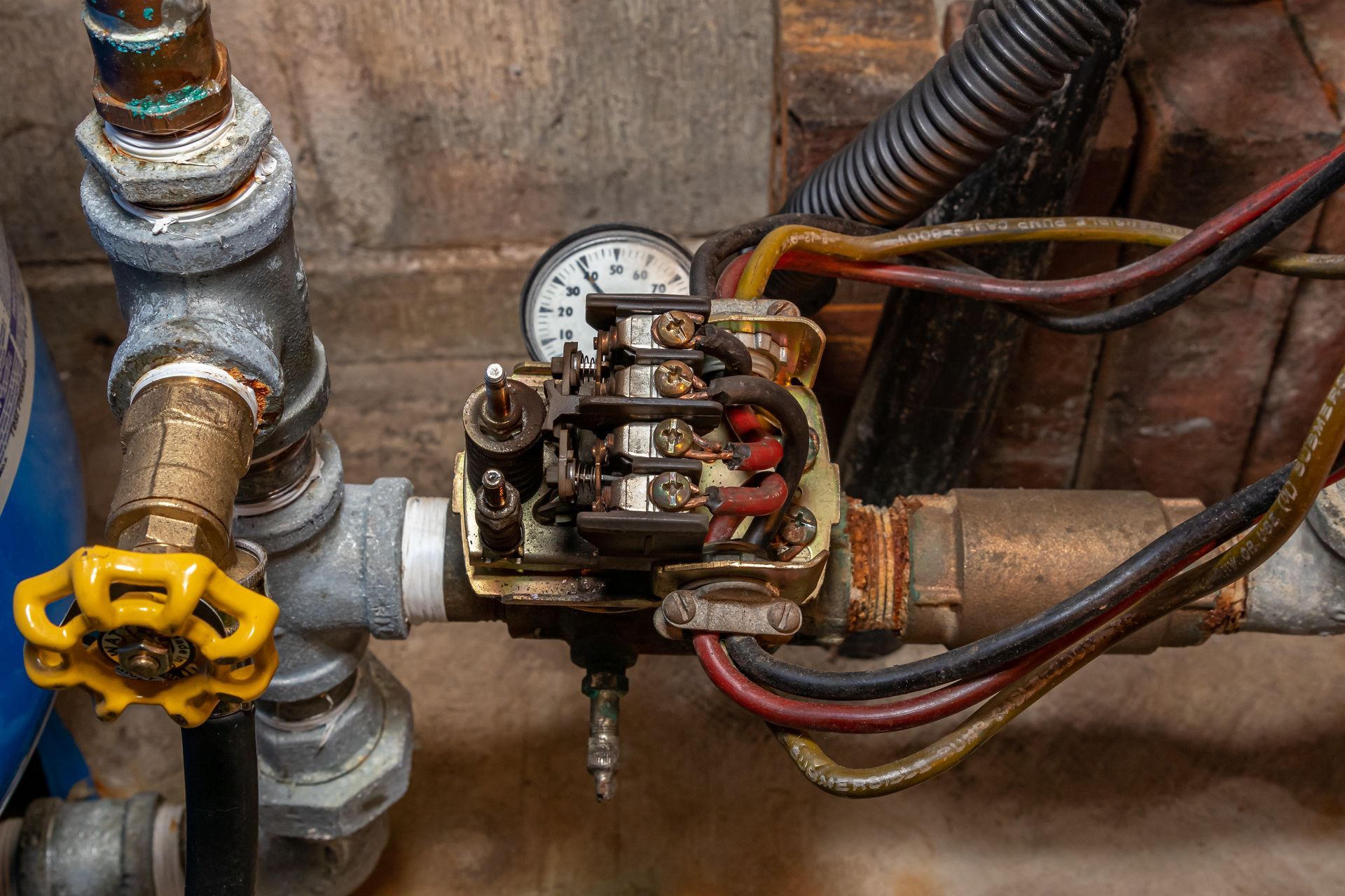 Close-up of a gas valve and exposed pressure regulator with wires and pipes on a brick wall
