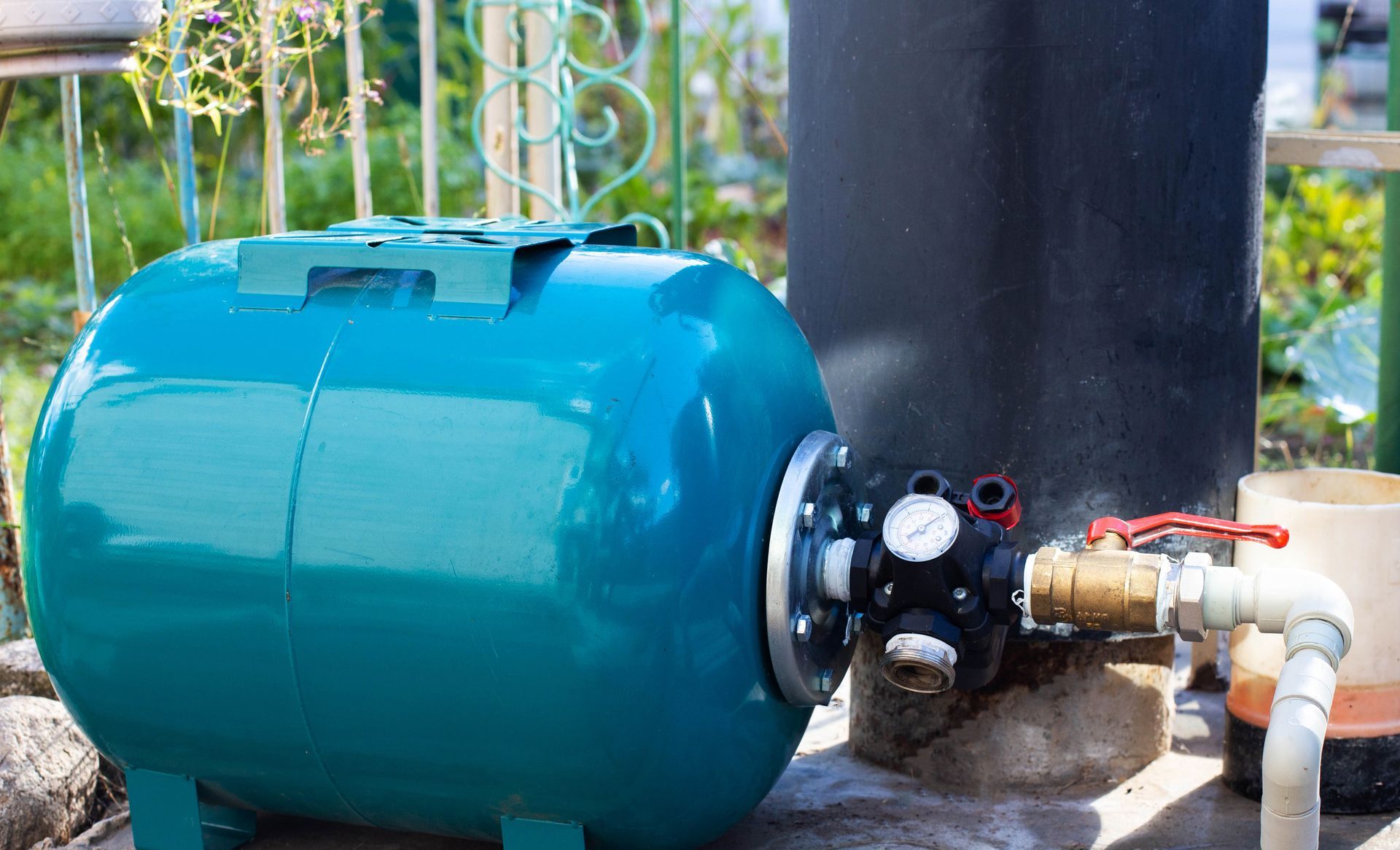 Blue pressure tank with pump and pipes outdoors near a concrete wall