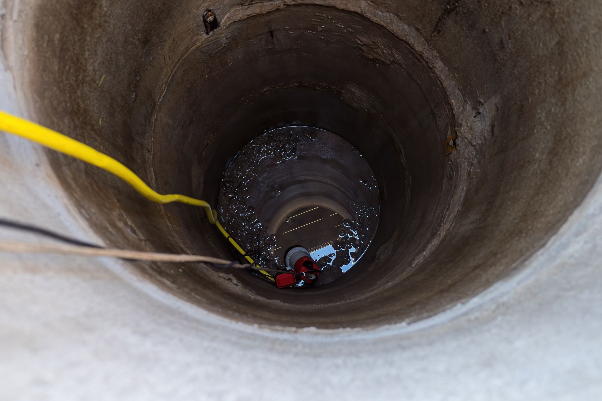 Person climbing down a deep concrete well with a rope, viewed from above.