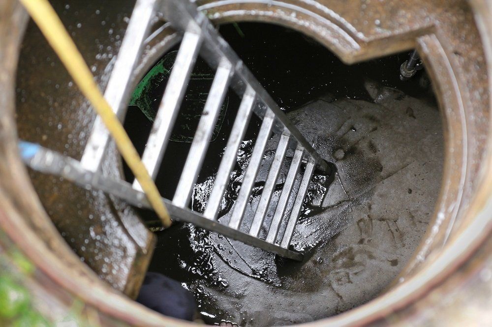 Open manhole with a metal ladder descending into a dark, wet sewer opening
