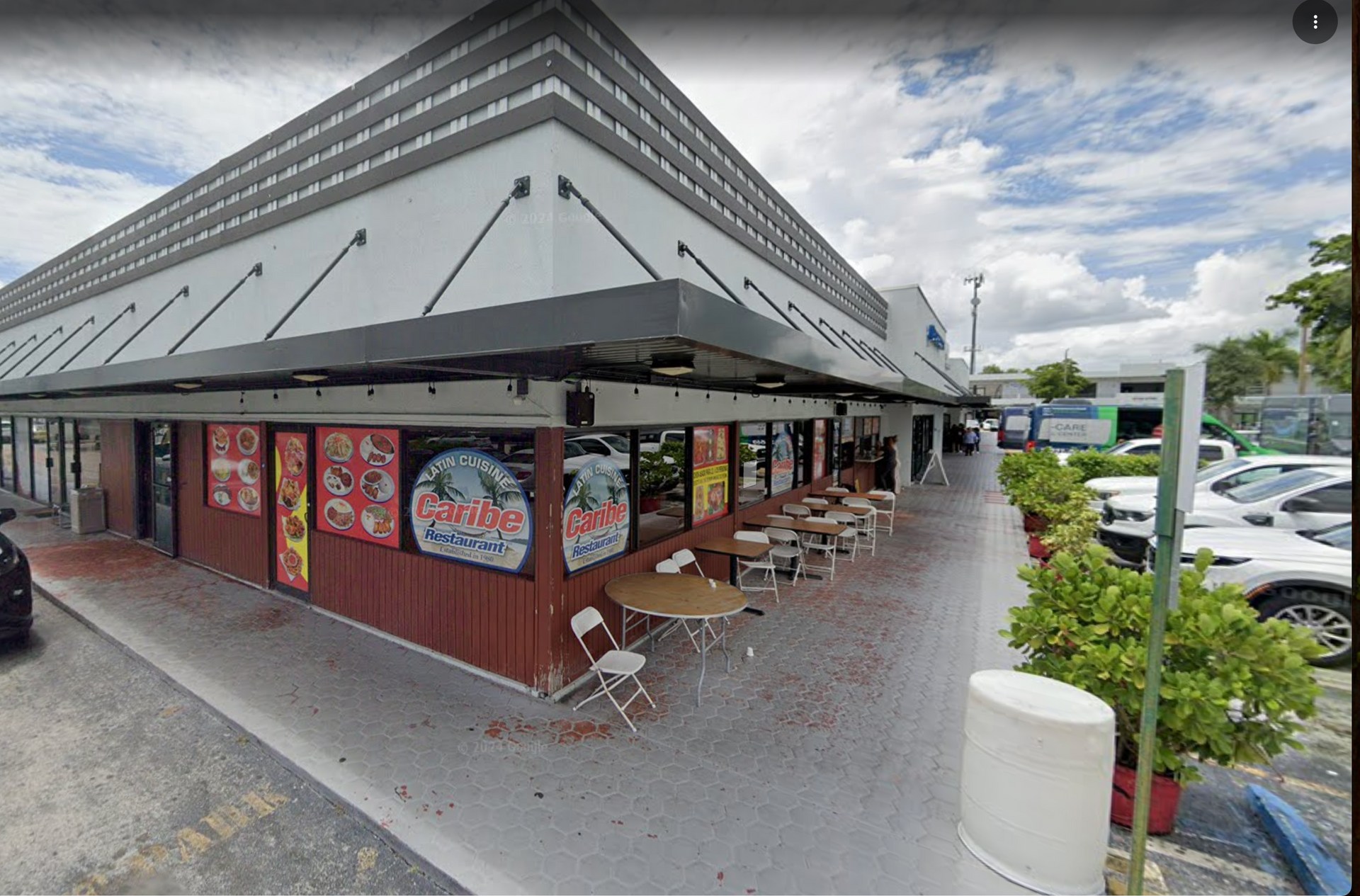 A restaurant with outdoor seating under a gray awning. Red siding and colorful signs adorn the facade.
