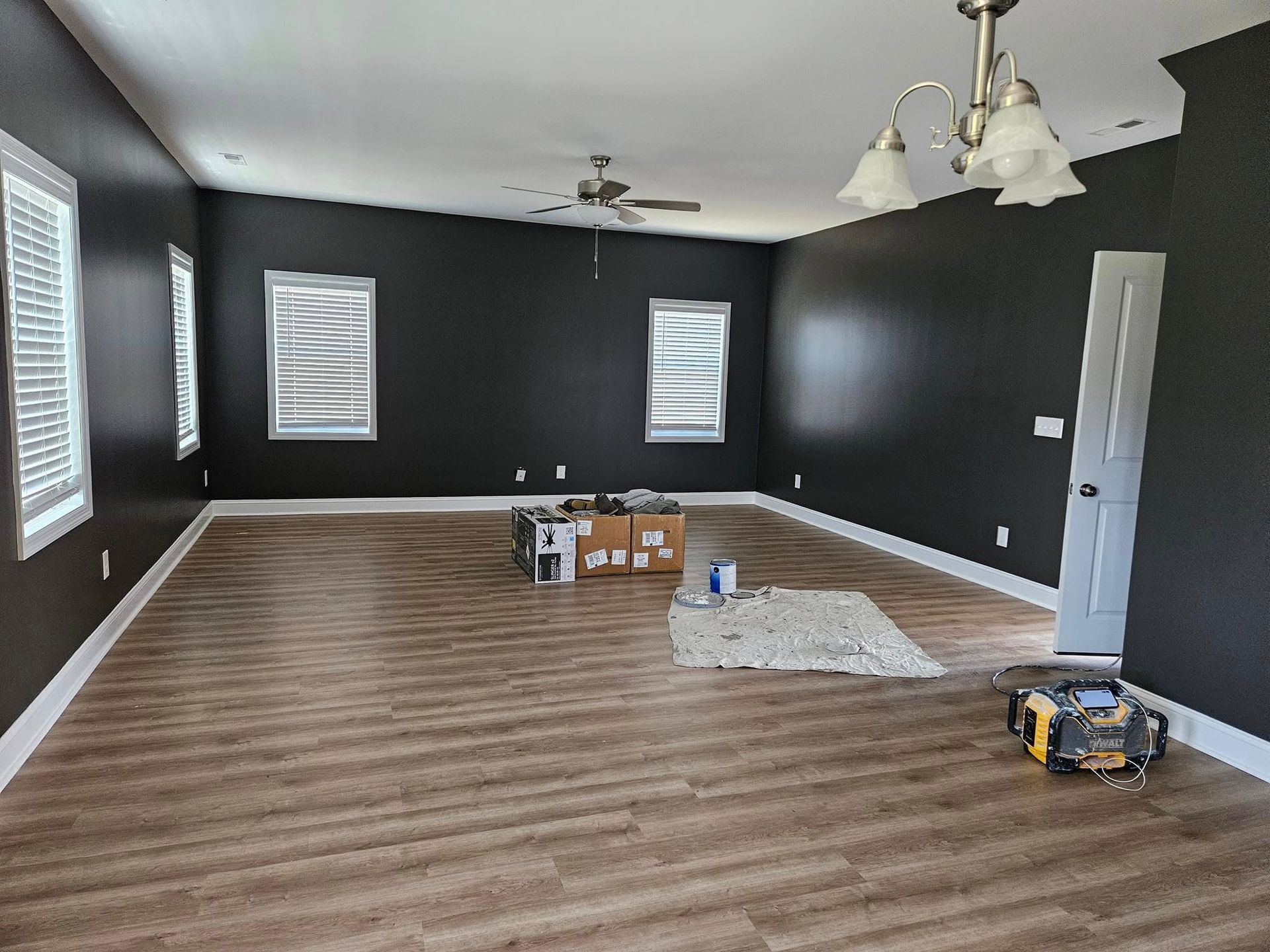 A living room with black walls and wooden floors is being painted.