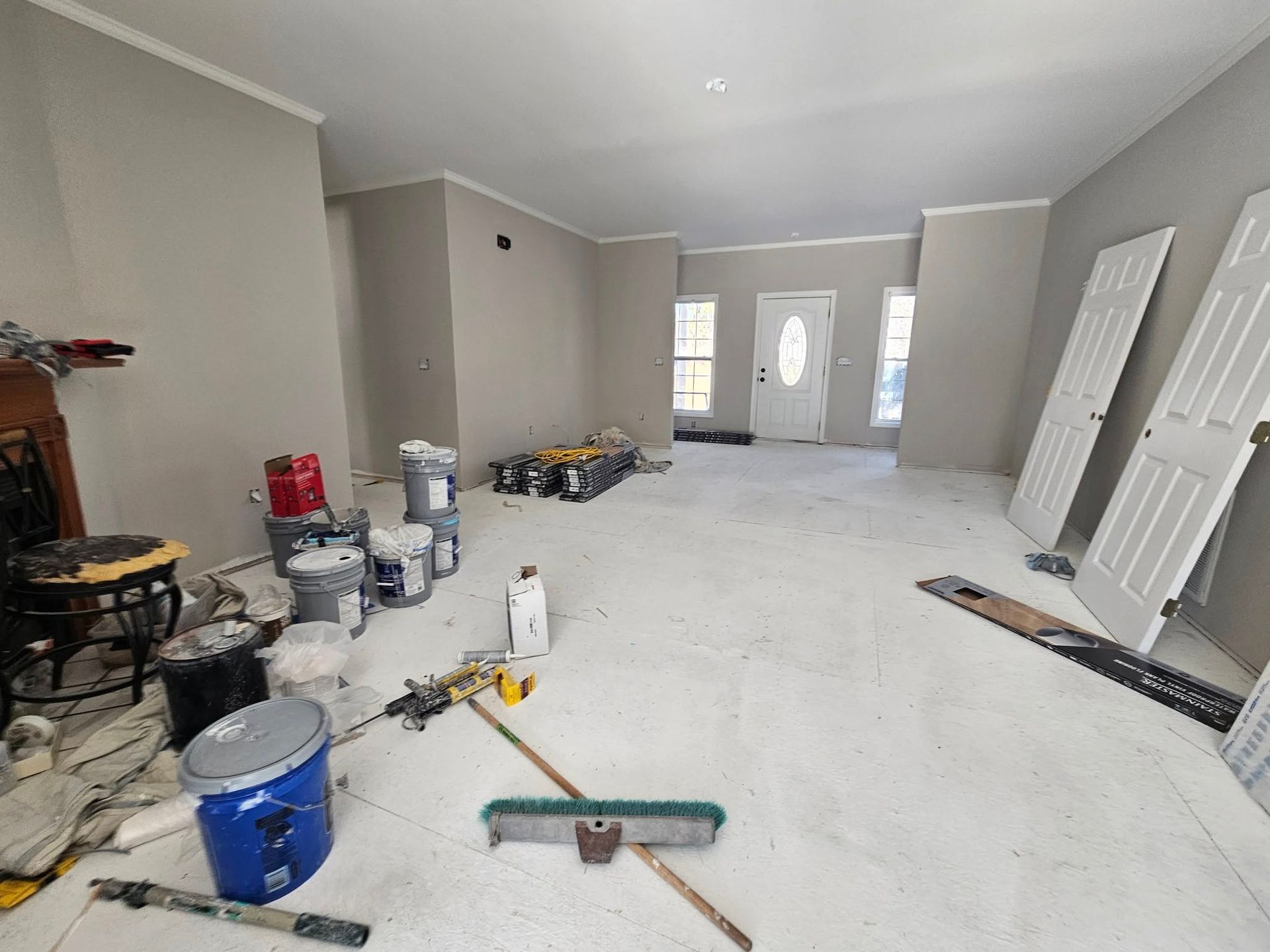 A room that is being painted with buckets of paint and a broom.