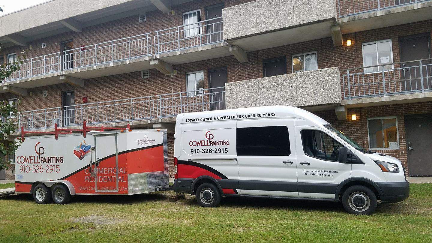 A white van with a trailer attached to it is parked in front of a building.