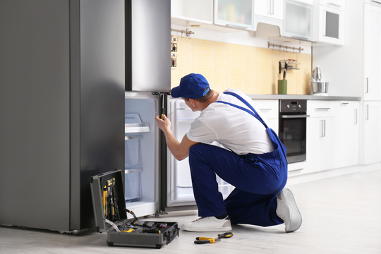 A man is repairing a refrigerator in a kitchen.