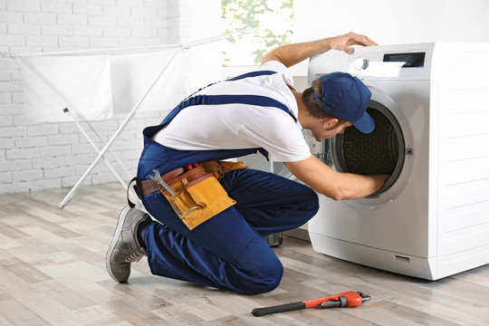 A man is fixing a washing machine in a room.