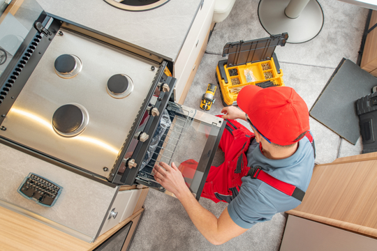 A man is working on a stove in a kitchen.