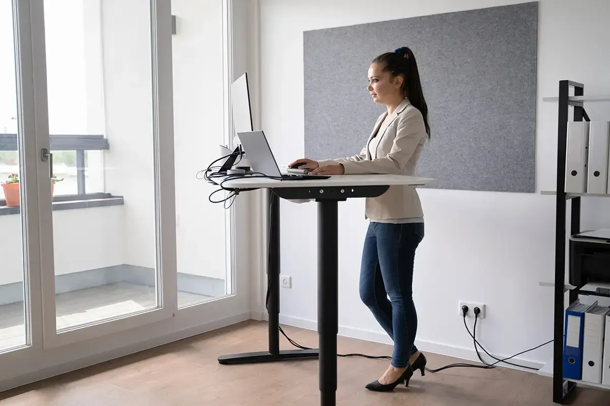 Een vrouw is aan het werk aan een ergonomisch elektrisch zit/sta bureau