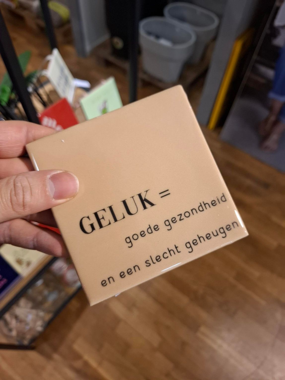 Hand holding a beige card with Dutch text, “GELUK = goede gezondheid en een slecht geheugen.”