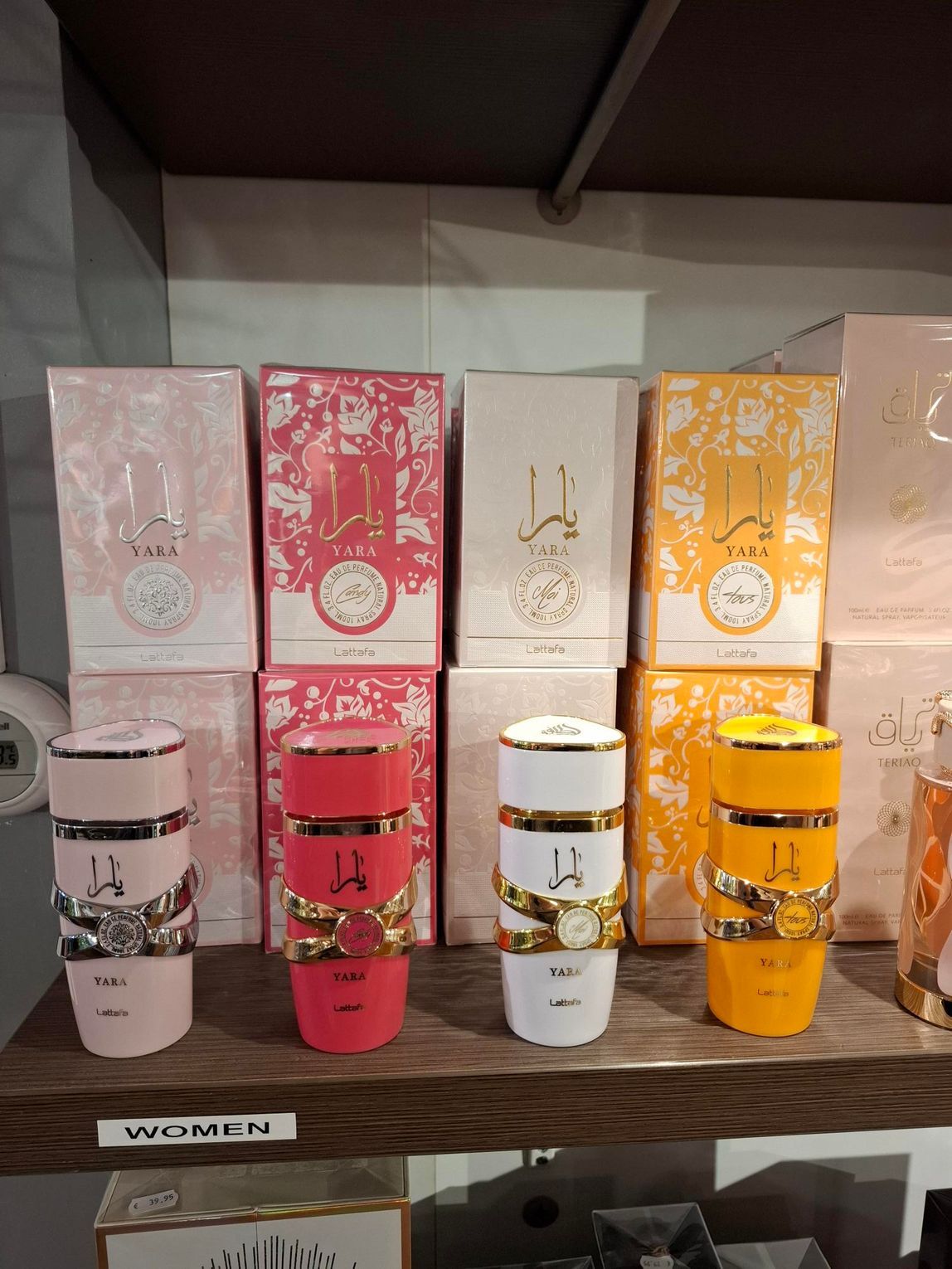 Parfumflesjes in roze, rood, wit en geel staan ​​uitgestald op een houten plank in een winkel.