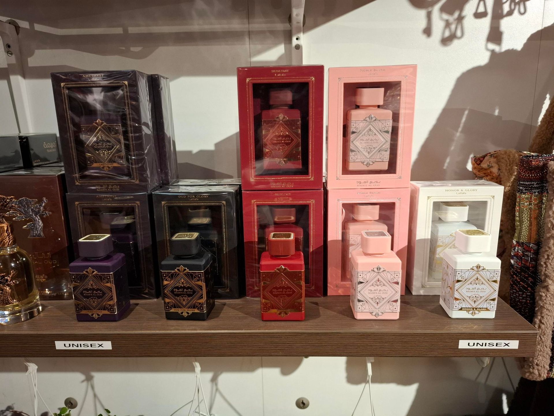 Op een houten plank staan ​​diverse parfumflesjes, zowel in als zonder verpakking, in verschillende kleuren, waaronder paars, zwart, rood en roze.