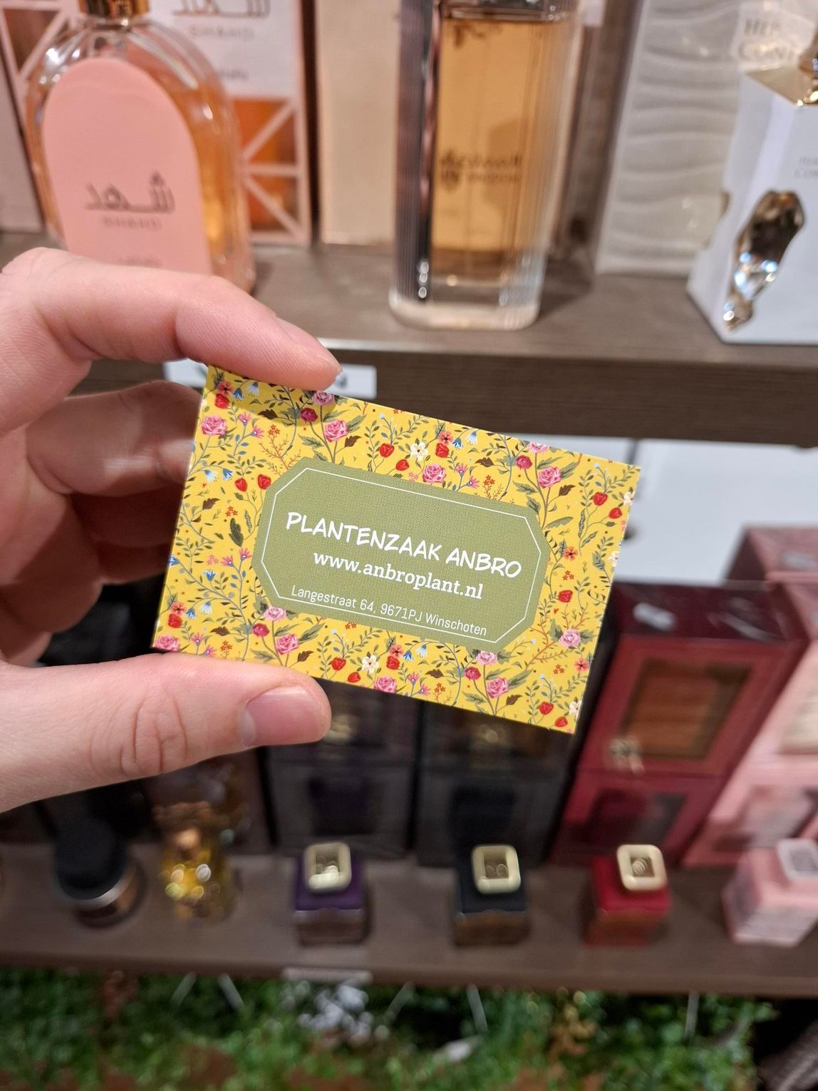 Een hand houdt een geel visitekaartje met bloemenmotief van 