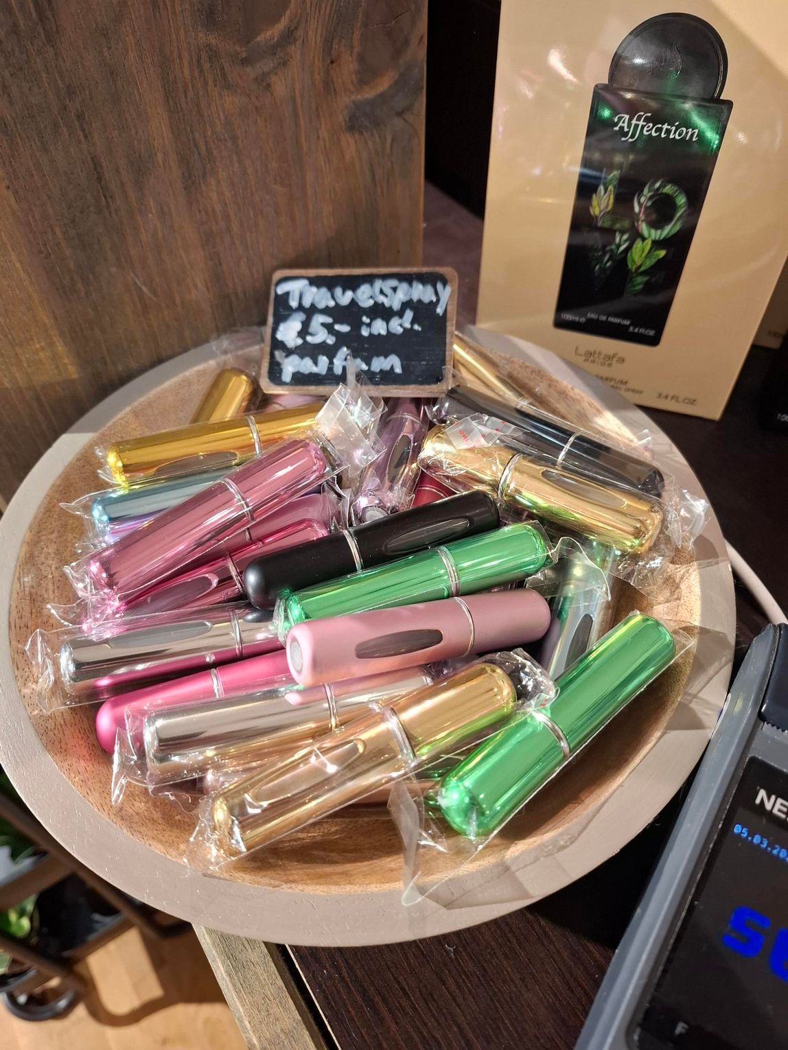 Een hand houdt twee kleine, cilindrische parfumverstuivers vast: een roze en een zwarte, beide met een verticaal kijkvenster.