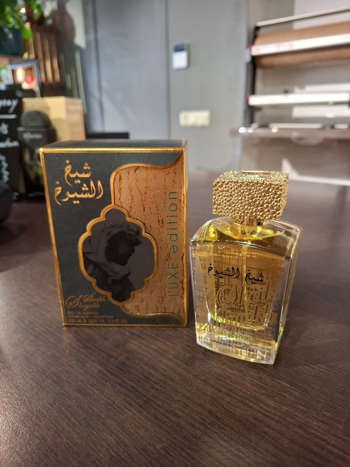 Een flesje Sheikh Al Shuyukh Luxe Edition parfum naast de zwart-gouden doos op een houten ondergrond.