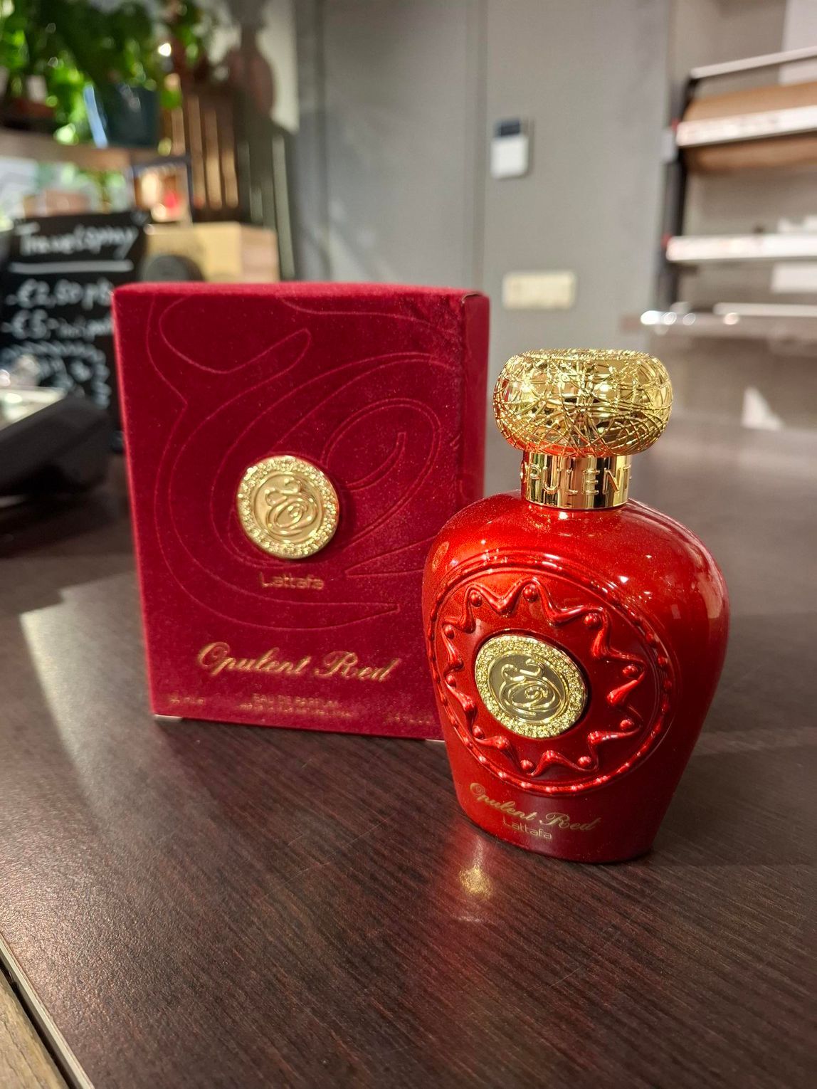 Een rode parfumfles en de bijbehorende rode fluwelen doos met gouden ronde emblemen staan ​​op een donkere houten tafel.