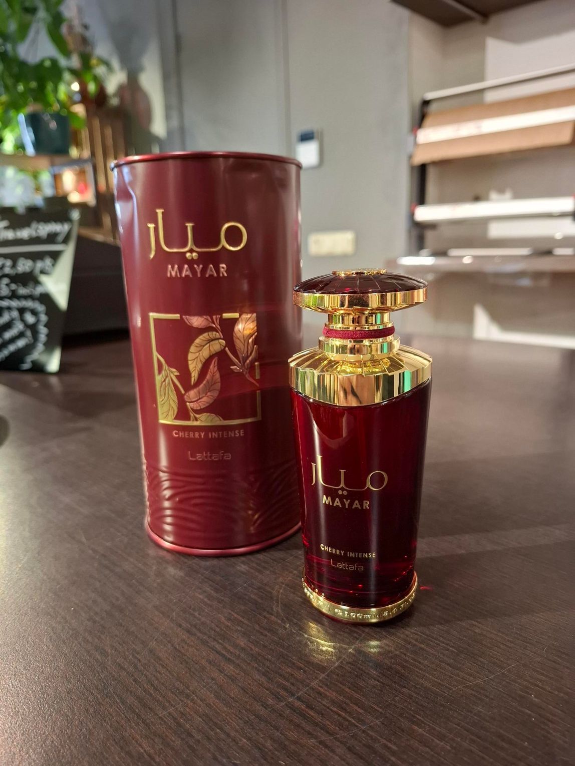 Een bordeauxrode parfumfles en het bijbehorende cilindervormige blikken doosje staan ​​op een donkerhouten ondergrond.