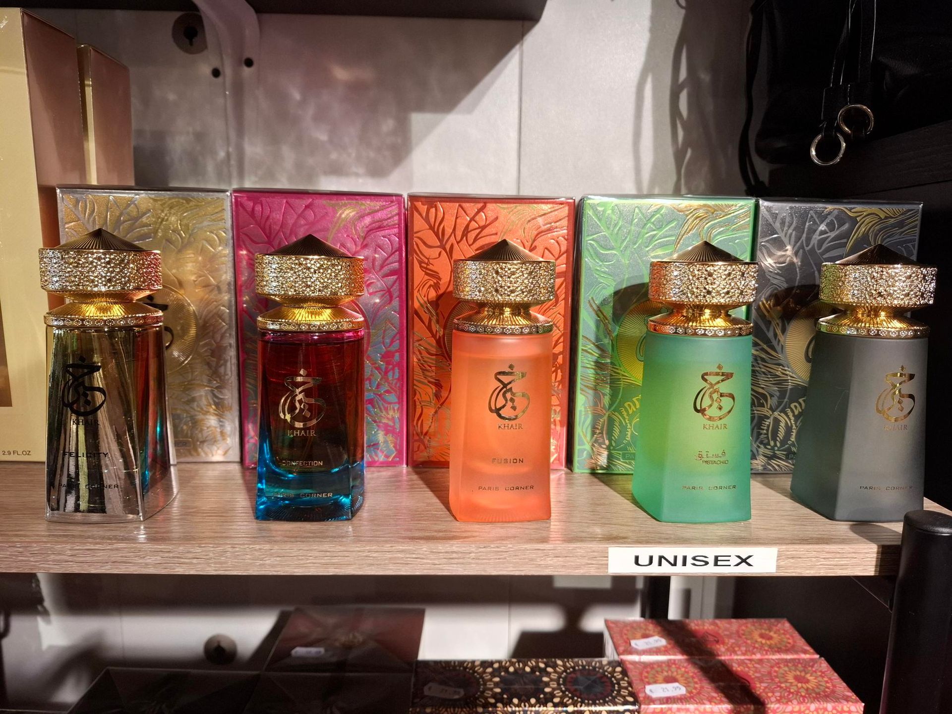 Vijf parfumflesjes in kleurverloop – goud, rood, oranje, groen en grijs – staan ​​op een rij in een winkelschap.