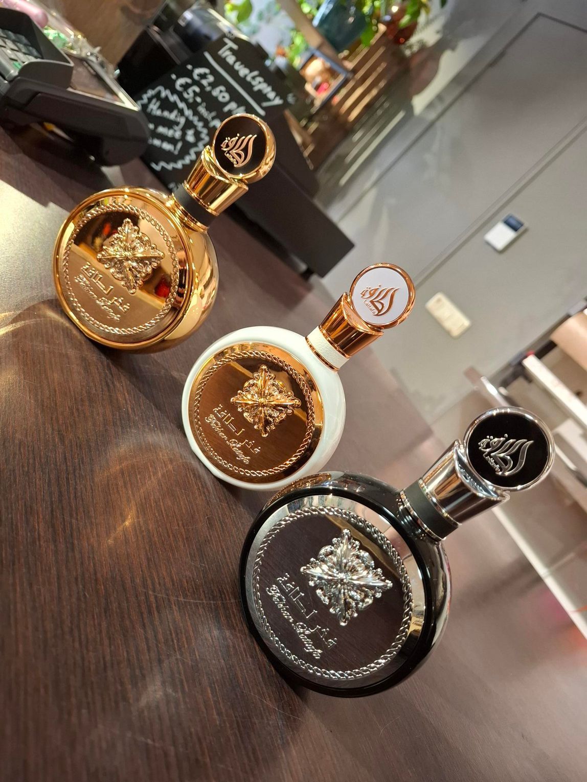 Drie ronde parfumflesjes met gouden en zilveren accenten staan ​​op een houten ondergrond.