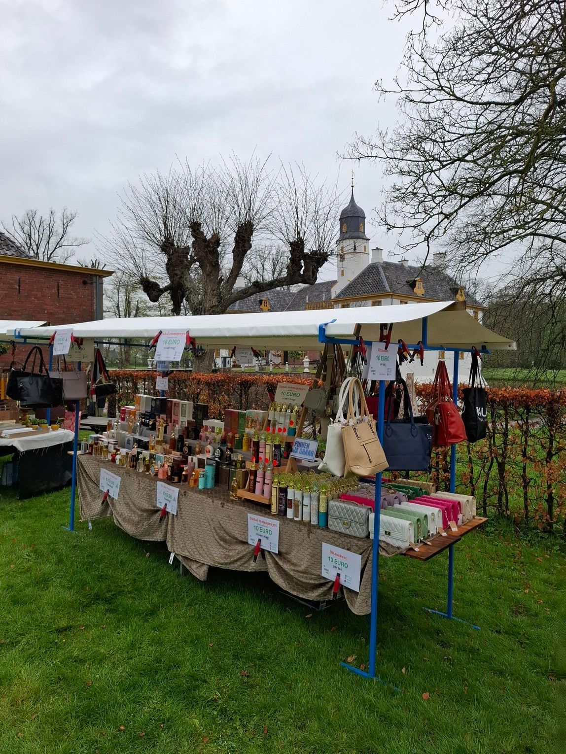 Een marktkraam met tassen en diverse artikelen uitgestald op een tafel buiten voor een gebouw dat op een kerk lijkt.