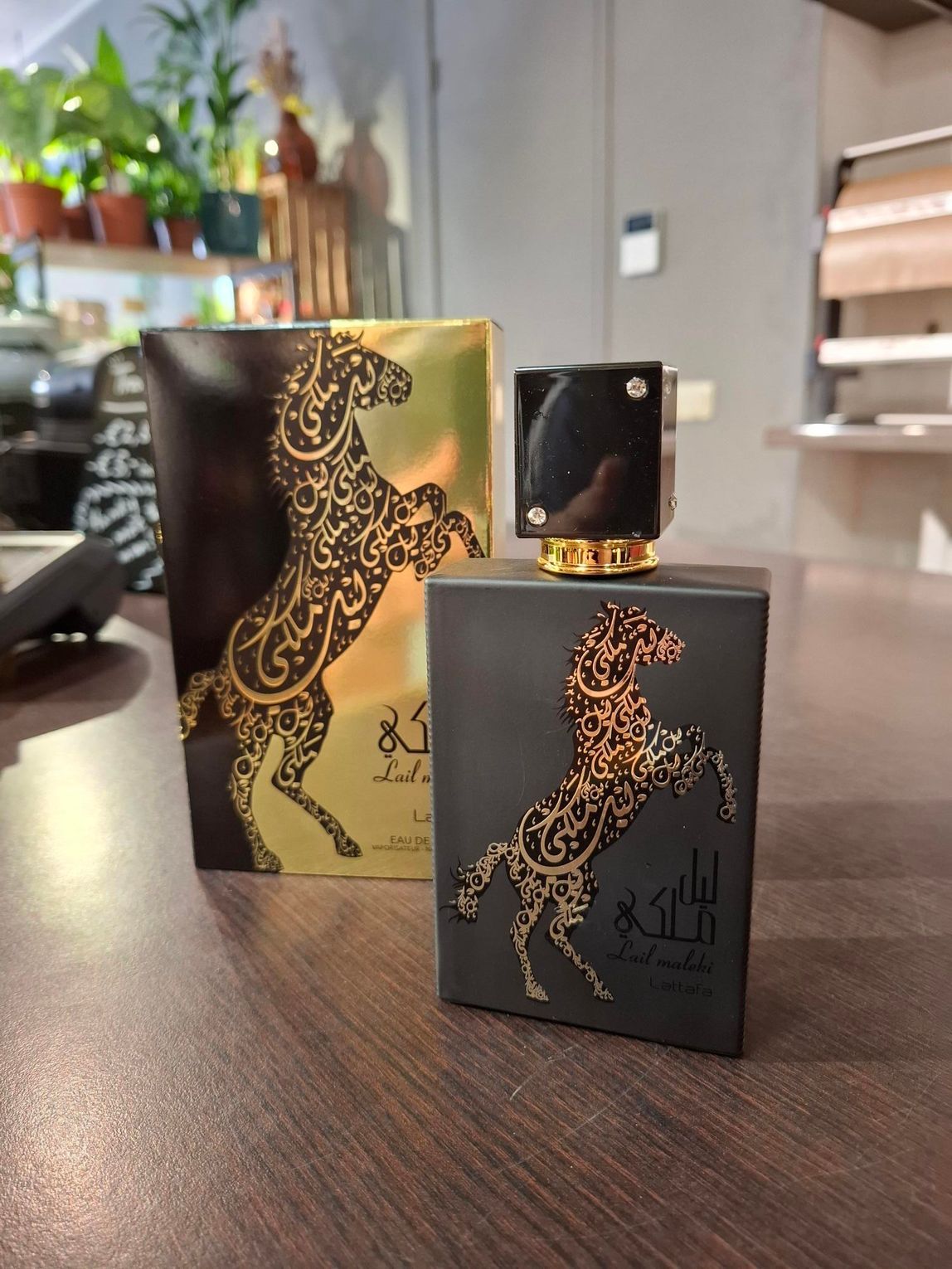 Een zwarte parfumfles en de bijbehorende gouden doos, beide met een decoratieve gouden paardensilhouet, staan ​​op een houten ondergrond.