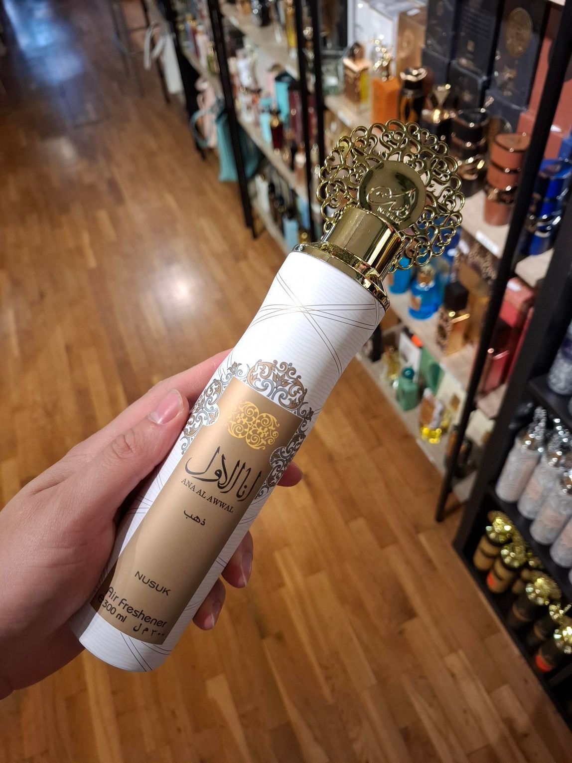 Een persoon houdt een sierlijke wit-gouden fles Arabisch parfum vast tegen een wazige achtergrond van winkelschappen.