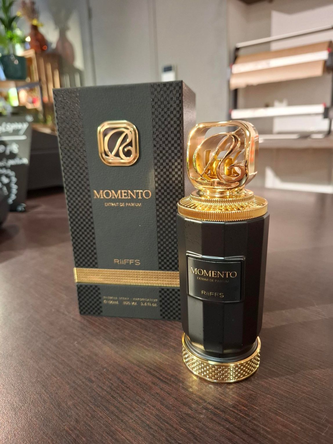Een zwart-gouden parfumflesje met een gestructureerde dop staat naast de bijpassende zwarte doos op een donkerhouten ondergrond.