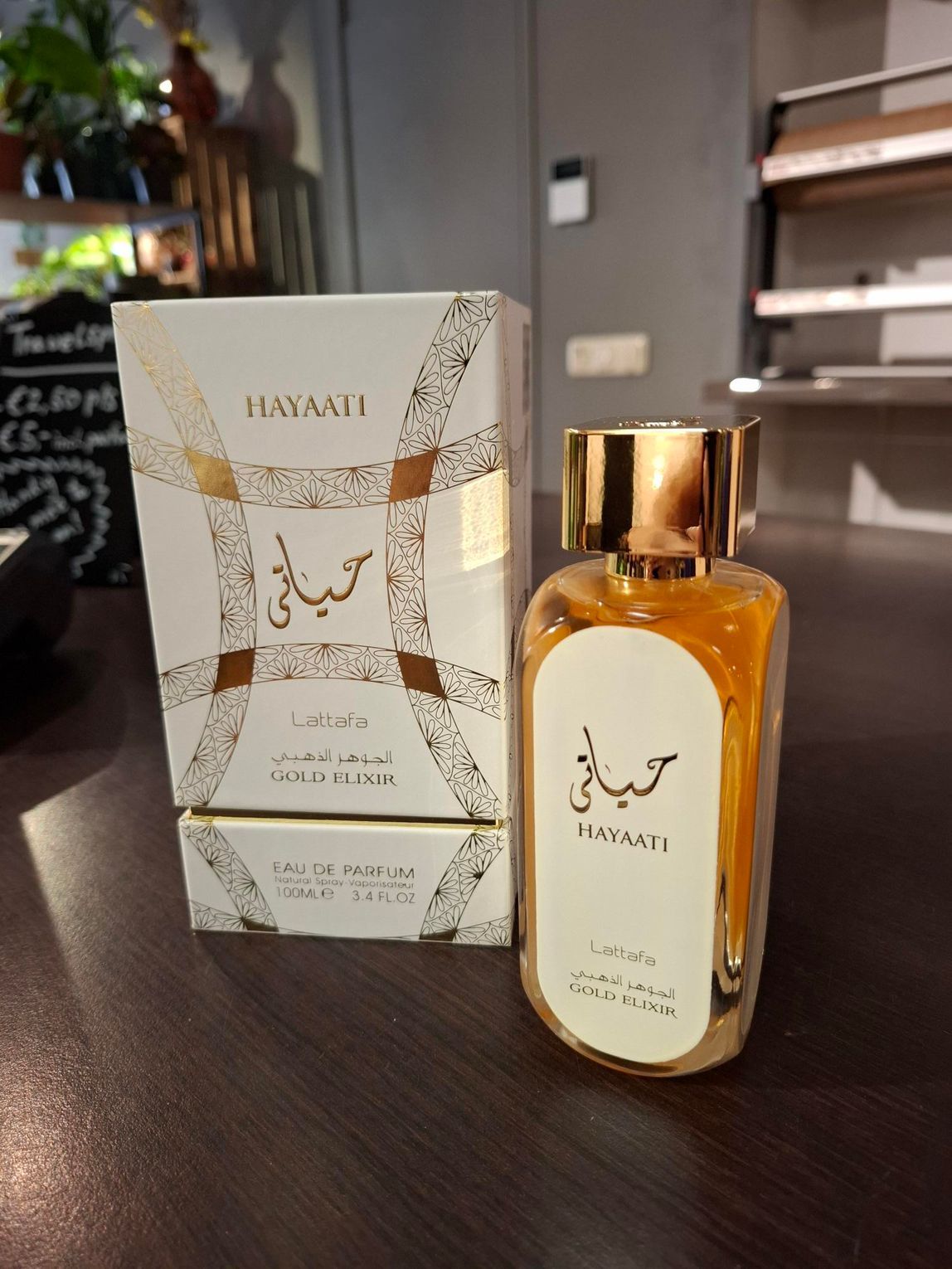 Een fles en doos Hayaati-parfum met gouden accenten op een crèmekleurige achtergrond, staand op een donkere ondergrond.