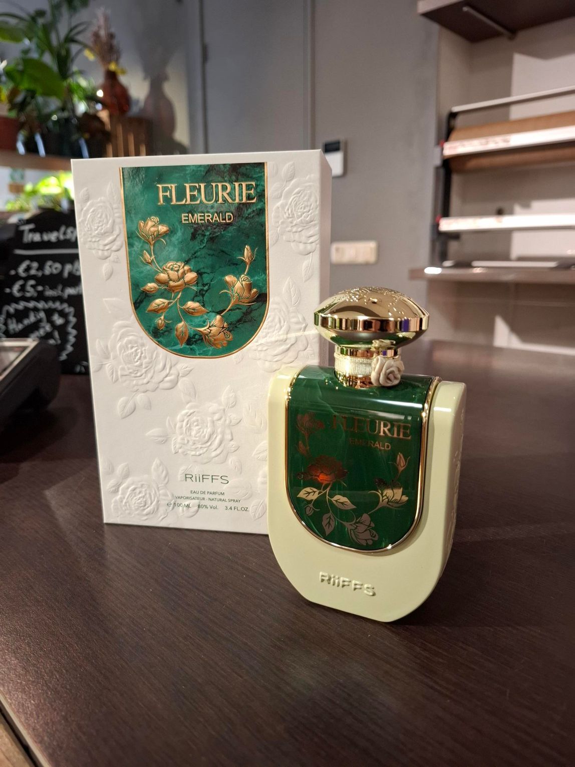 Een flesje Fleurie-parfum en de bijbehorende witte doos met bloemenmotief staan ​​op een donkerhouten ondergrond.