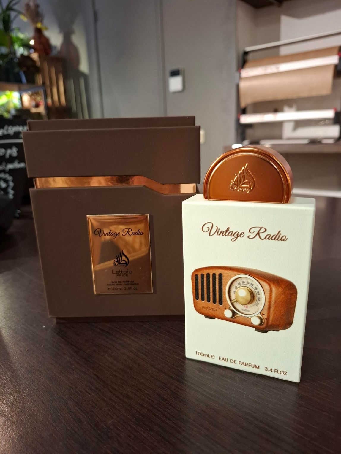 Een bruine, rechthoekige parfumdoos naast een verticale witte doos met een afbeelding van een vintage radio.