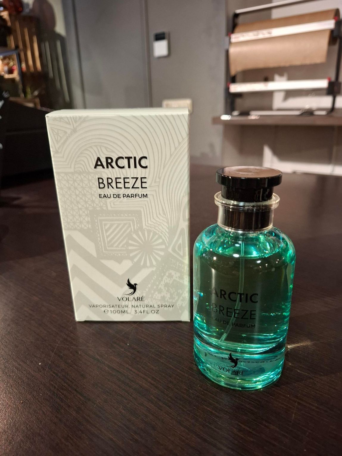 Een doos en een fles Arctic Breeze eau de parfum op een donkerhouten oppervlak in een schemerig verlichte kamer.