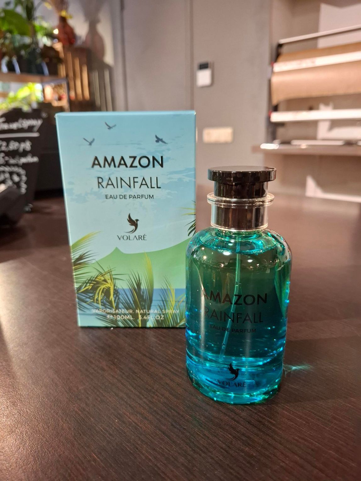 Een flesje Amazon Rainfall-parfum en de bijbehorende doos, met een turquoise, tropisch design, staan ​​op een houten ondergrond.