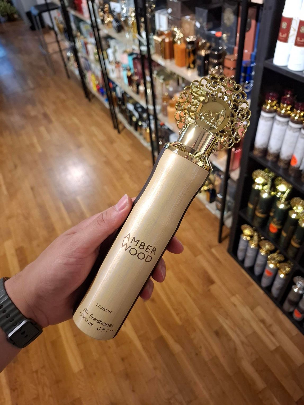 In een parfumerie houdt een hand een hoge, cilindrische fles vast met het opschrift 