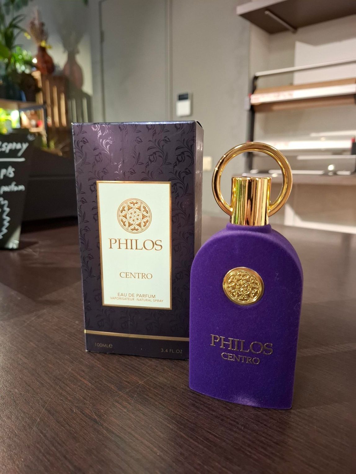 Een paarse, met fluweel beklede fles Philos Como-parfum staat naast de bijpassende donkerpaarse doos op een houten ondergrond.