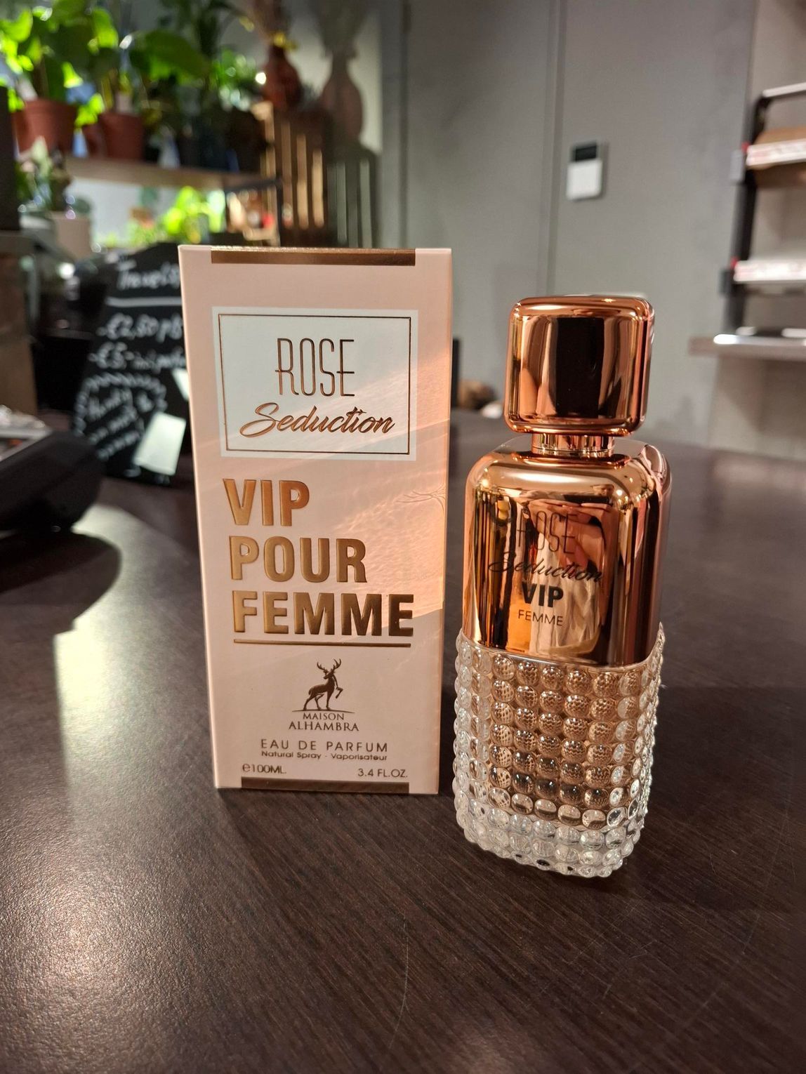 Een flesje Rose Seduction VIP Pour Femme parfum naast de lichtroze doos op een donkere ondergrond.