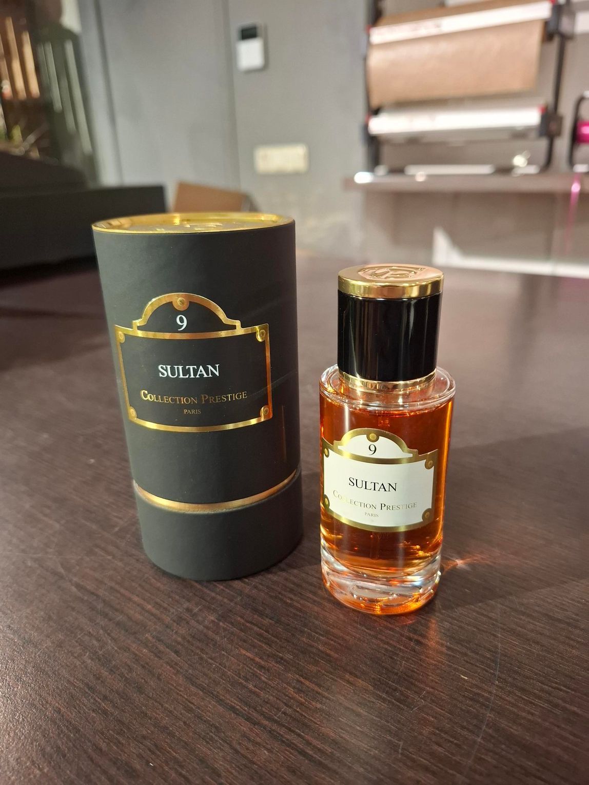 Een flesje Sultan oud parfum met de bijbehorende cilindrische, zwart-gouden etui, staand op een houten ondergrond.