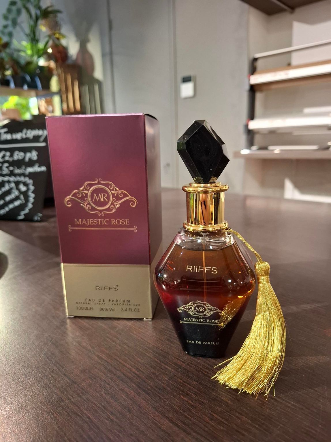 Een flesje Majestic Rose parfum met een gouden kwastje en de bijpassende bordeauxrode en gouden doos op een houten ondergrond.