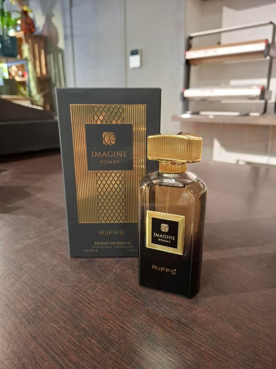 Een flesje Imagine-parfum met de donkergrijze en gouden doos, geplaatst op een bruine houten ondergrond.