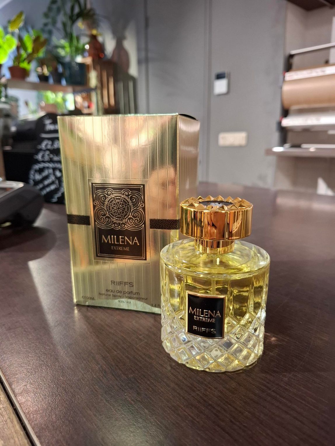 Een gouden parfumdoosje staat achter een parfumflesje van kristalgeslepen glas met een gouden dop op een donkerhouten ondergrond.